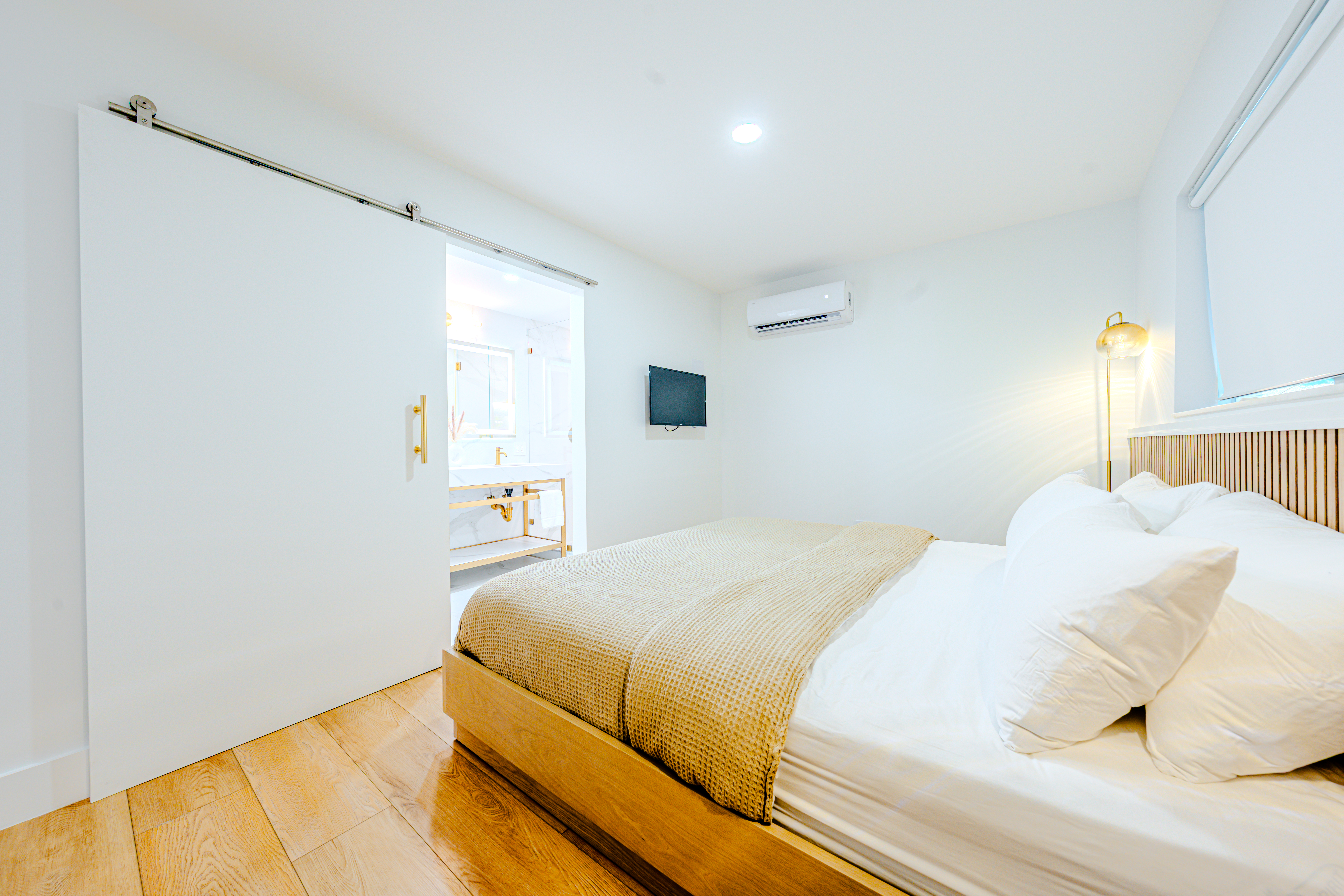 A bright and clean hotel room with a bed, window, lamp, and TV.
