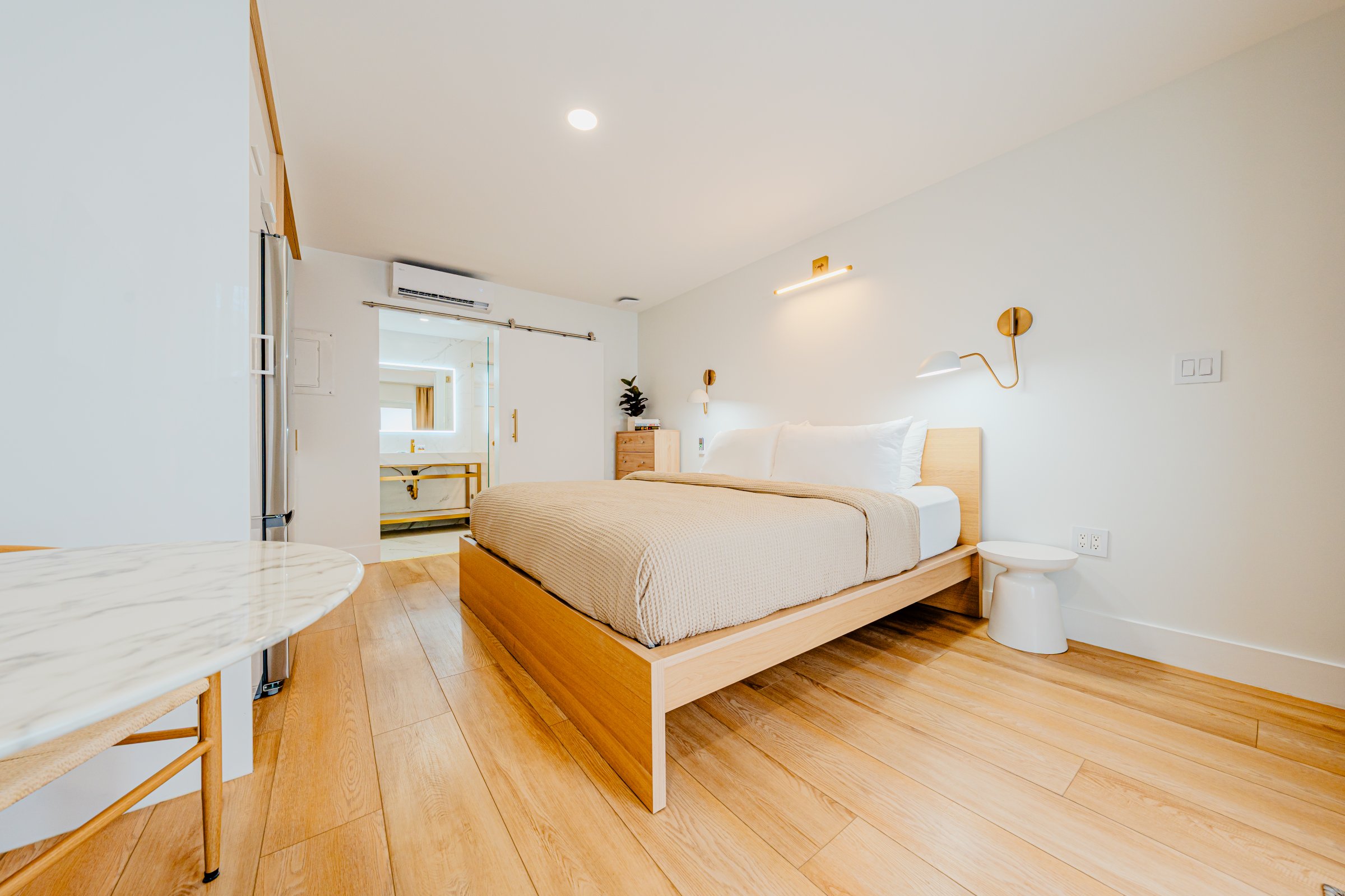 A bright and airy hotel room with a bed, table, and doorway.