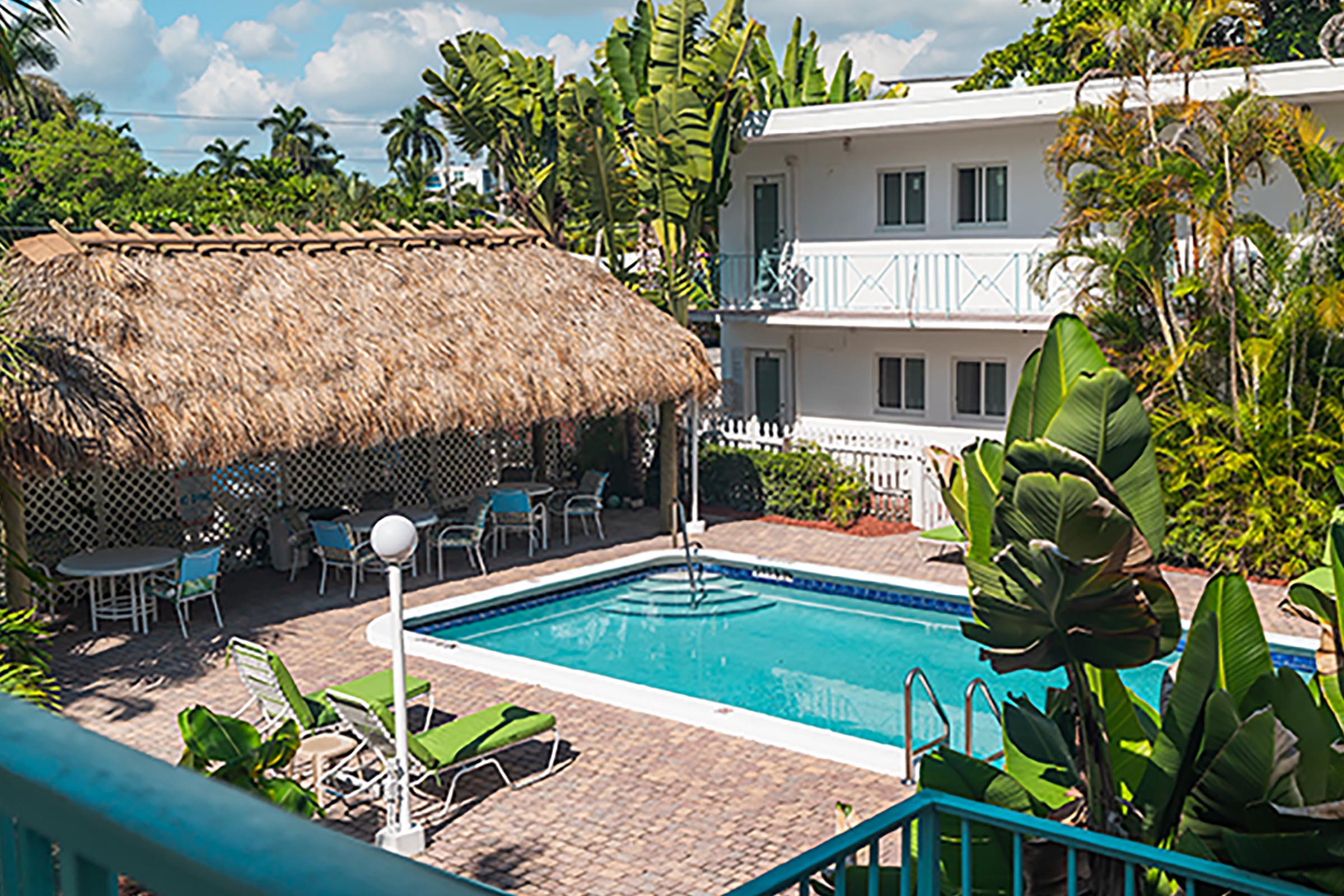 A swimming pool with a thatched roof structure and a white building in the background.