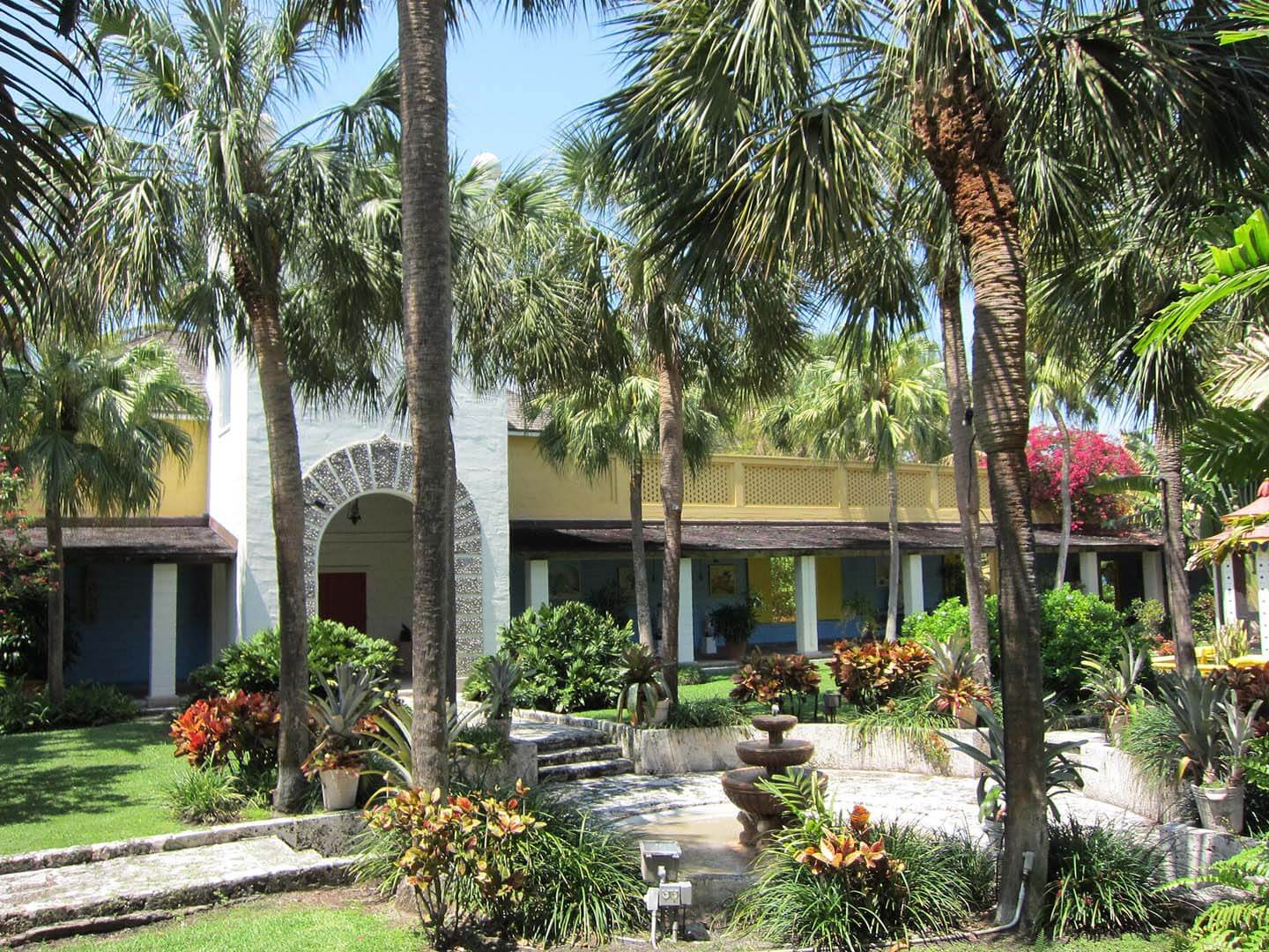 A tropical exterior view of a building with a fountain and palm trees.