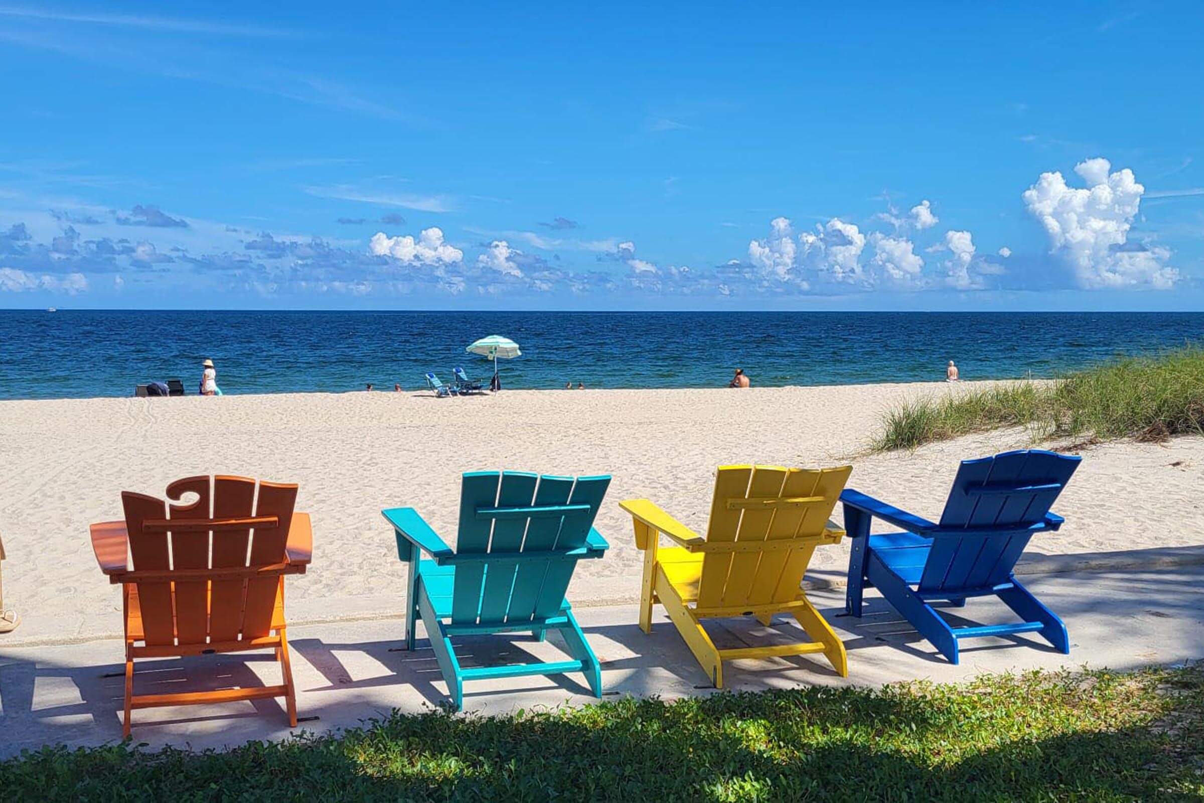 Four colorful beach chairs face the ocean on a sandy beach.